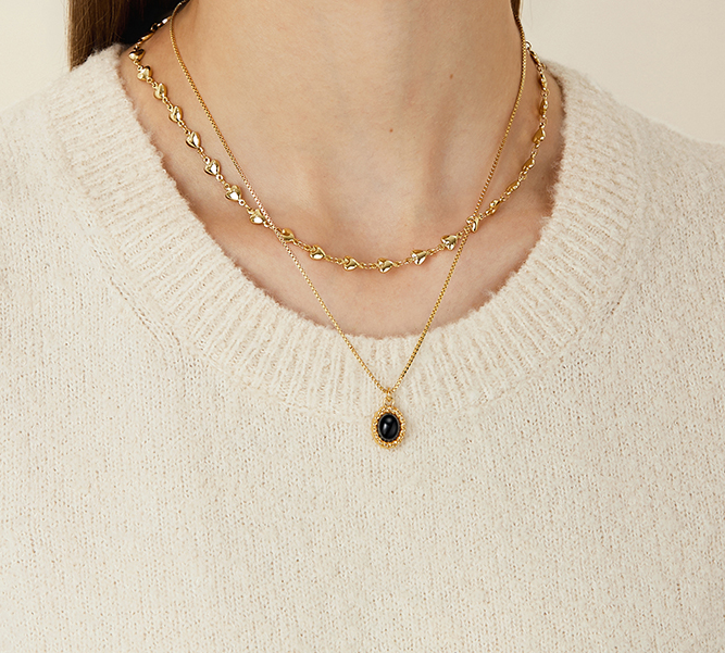 Close-up of a woman’s neck featuring two layered gold necklaces, one with a black gemstone pendant, against a cozy cream sweater.