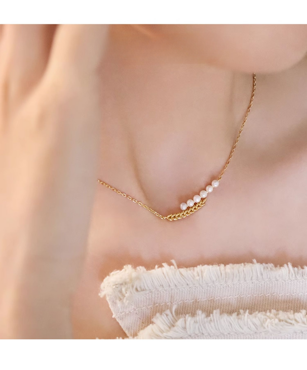 Close-up of a woman wearing a delicate gold necklace adorned with small pearls, accentuating her neckline.