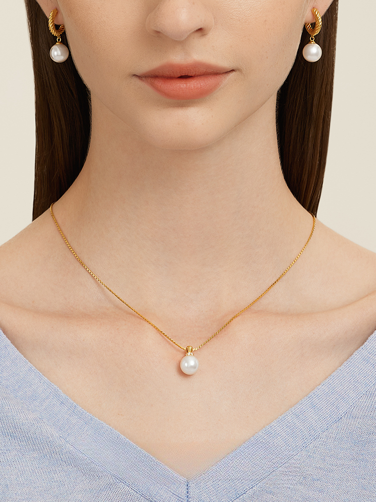 A close-up of a delicate gold necklace with pearls, elegantly resting on a person's collarbone, partially obscured by their hand.